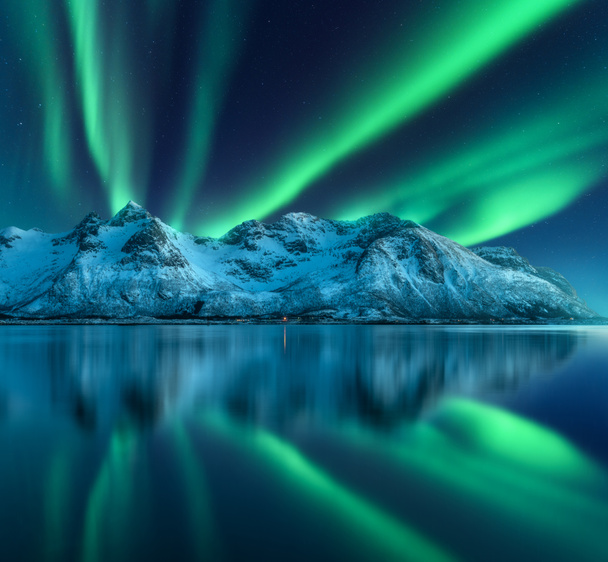 Північне сяйво над сніжними горами, морським узбережжям, відбивається у воді вночі в Лофотені, Норвегія. Aurora borealis і вкриті снігом скелі. Зимовий пейзаж з полярними вогнями і фіордом. Зоряне небо - Фото, зображення