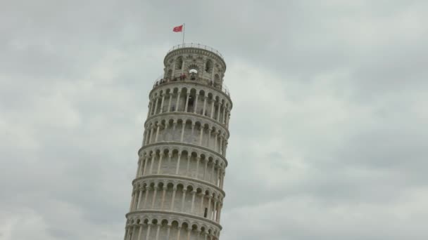 Pisan nojaava torni pilvistä taivasta vasten. Turistit ja Pisan tasavallan punainen lippu näkyvät huipulla, Italia. - Materiaali, video