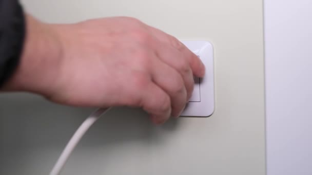 Egy emberi kéz lekapcsolja a háztartási készülékeket egy fehér konnektorról. Közelkép egy férfiról, aki kikapcsolja az elektromos berendezéseket egy szobában. Kiváló minőségű 4k videó - Felvétel, videó