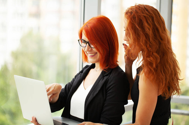 Две рыжие женщины работают вместе в современном офисе. - Фото, изображение