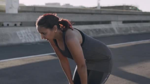 Ademend, moe en vrouw rennend in de straten van de stad voor fitness, marathontraining en motivatie voor lichaamsdoelen in Zweden. Adem, pauze en atleet op de weg na een cardiotraining voor de gezondheid. - Video