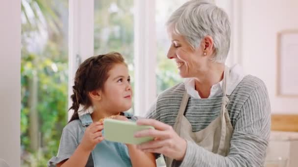 Telefon, süti és gyerekek egy lánnyal és nagymamával, akik a közösségi médiát használják családként az otthonukban. Streaming, mobil és a gyerekek egy női gyermek és idősebb nő kötődés a házban. - Felvétel, videó