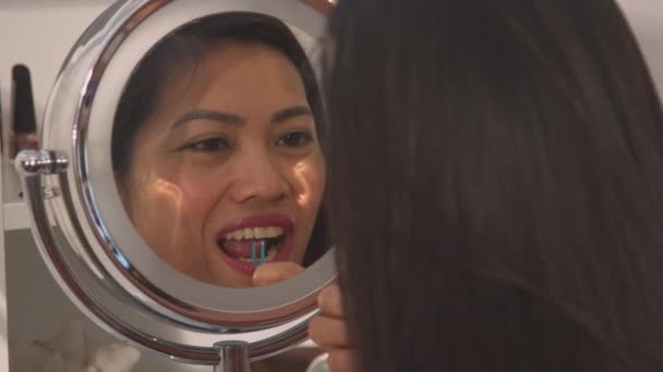 CHIUDI: Veduta di una bella donna in uno specchio cosmetico che filtra i suoi denti bianchi. Bella signorina che usa lo stuzzicadenti dentale per prendersi cura dell'igiene dentale. routine mattutina per mantenere un bel sorriso. - Filmati, video