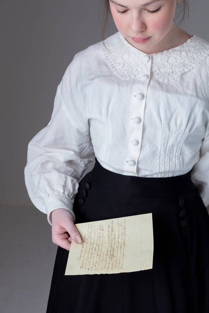 Eine junge viktorianische oder edwardische Frau trägt eine weiße Garibaldi-Bluse aus Leinen und schwarzen Rock und hält einen Brief in der Hand - Foto, Bild