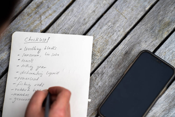 gril writing a camping list in a piece of paper. writing a check list with a pencil and a phone - Foto, Imagen