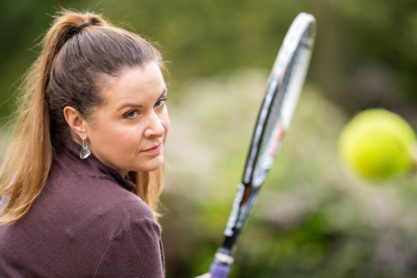 Kadın tenis oyuncusu İngiltere 'de çimen kortunda ön el antrenmanı yapıyor ve tenis toplarına vuruyor. - Fotoğraf, Görsel