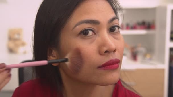PORTRAIT Hermosa mujer asiática que aplica bronceador en polvo para terminar su look de maquillaje. Jovencita alegre siendo complacida después de terminar su maquillaje. Persona femenina aplicando contorno para maquillarse las mejillas - Imágenes, Vídeo