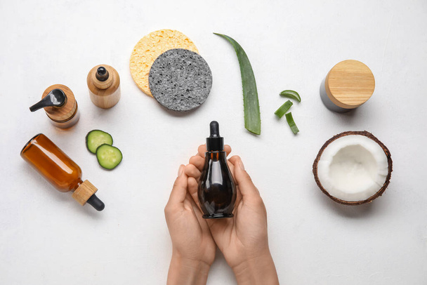 Dámské ruce s lahví esenciálního oleje, kosmetiky, přírodních ingrediencí a houbiček na světlém pozadí - Fotografie, Obrázek