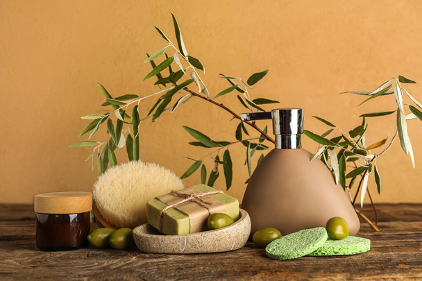 Natuurlijke cosmetica met groene olijven, sponzen, massageborstel en takken op tafel bij beige wand - Foto, afbeelding