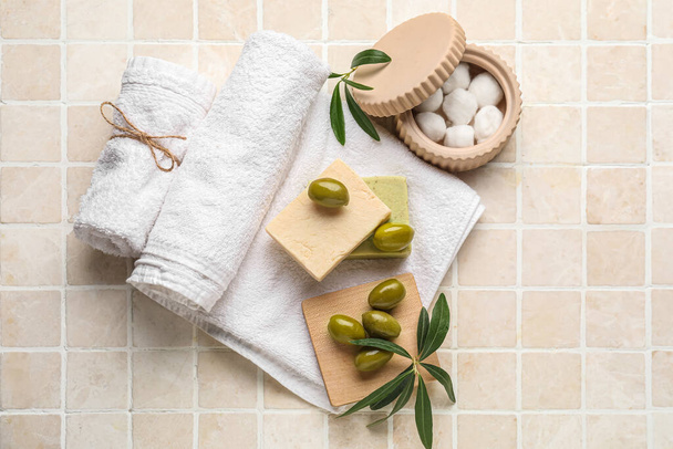 Handdoeken met zeep, groene olijven, takken en katoenen ballen op beige tegelondergrond - Foto, afbeelding