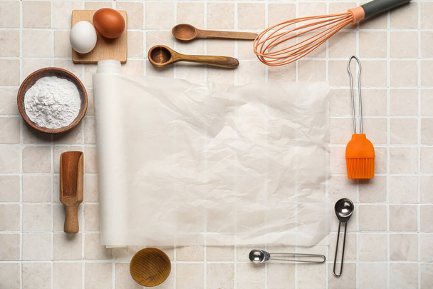 Papel de panificação com utensílios de cozinha, farinha e ovos sobre fundo azulejo bege - Foto, Imagem