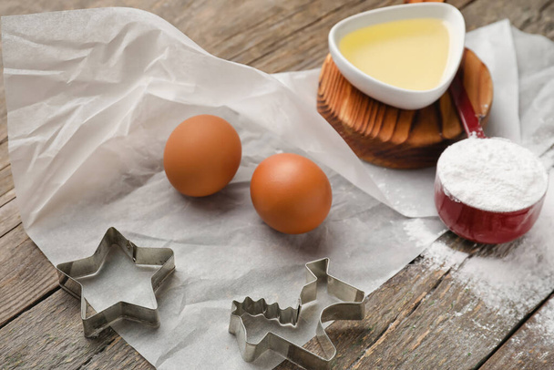 Ahşap zemin üzerinde yumurta, yağ, un ve kurabiye keskisi olan kağıt fırını. - Fotoğraf, Görsel
