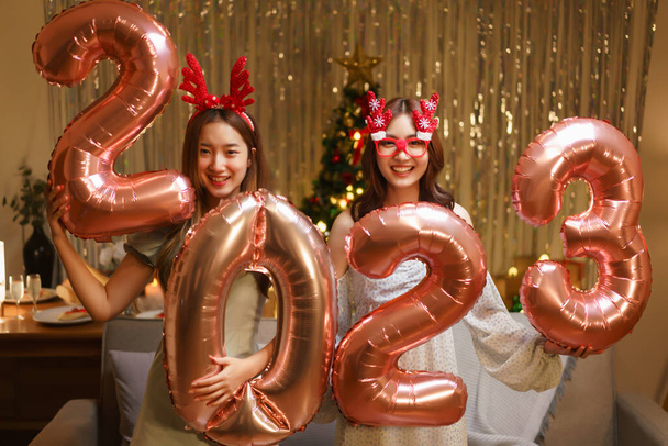 Yeni yıl partisi konsepti, iki güzel kadın yeni yıl partisinde 2023 numaralı pembe altın balonu tutuyor.. - Fotoğraf, Görsel