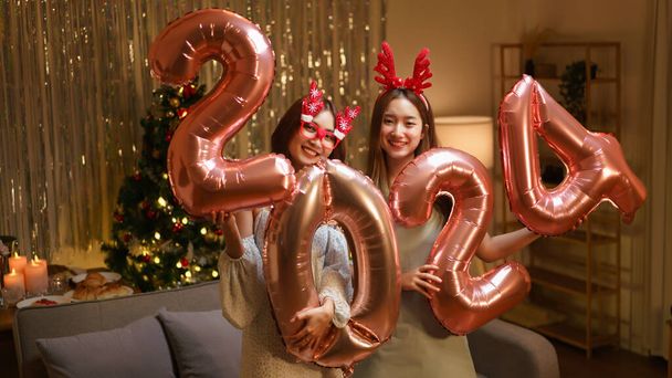 Nuovo concetto di celebrazione anno, Due belle donne che tengono palloncino numero 2024 in oro rosa in festa. - Foto, immagini