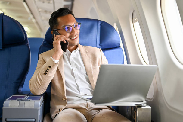 Sikeres és okos ázsiai üzletember telefonál az üzleti ügyfelével egy tengerentúli üzleti megbeszélés során. repülőgép, magánrepülő, üzleti osztály - Fotó, kép