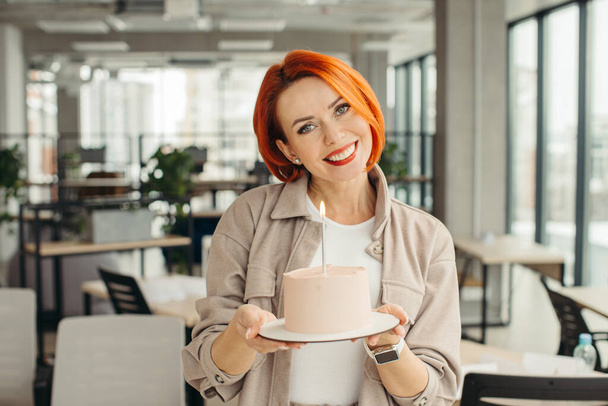 Щаслива бізнес-леді тримає торт на день народження, роблячи сюрприз вечірку зі своїми колегами в офісі
. - Фото, зображення