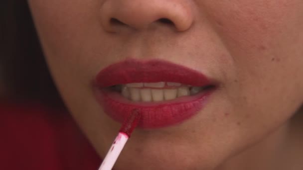 Részletes felvétel egy fiatal nőről, aki piros szájfényt használ az ajkain. Csinos fiatal hölgy színes és fényes ajakápolási termékkel. Női személy tökéletesíti a megjelenés, befejező smink kezelés. - Felvétel, videó