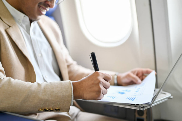 Uomo d'affari asiatico di successo gestisce i suoi documenti finanziari aziendali sul volo per il suo viaggio d'affari. primo piano, vista laterale immagine - Foto, immagini