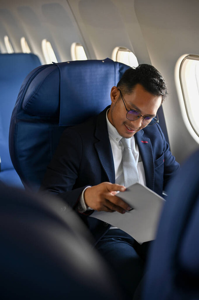 Portrait, homme d'affaires asiatique prospère en costume formel lisant les documents d'affaires pendant le vol vers sa destination. - Photo, image