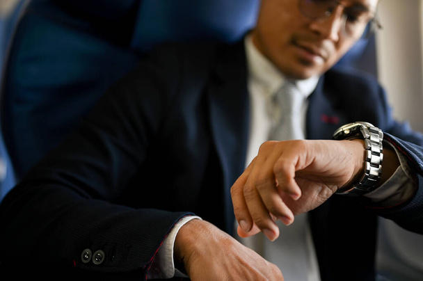 közeli kép, profi és sikeres ázsiai üzletember ellenőrzi az óráját az érkezés idejére. magánrepülő, magánrepülő. - Fotó, kép
