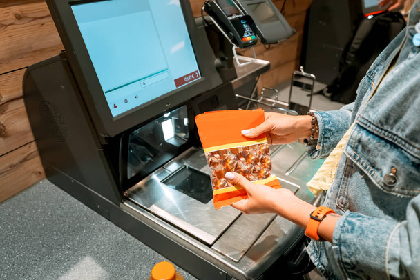 Eine Kundin scannt und bezahlt Waren aus einem Supermarkt an einem automatischen Selbstbedienungsterminal - Foto, Bild