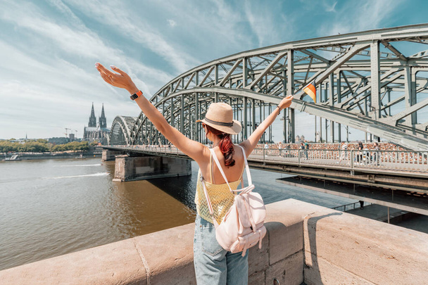 Chica feliz sosteniendo una bandera alemana contra el puente del Rin y la catedral de Colonia Dom. Lugares de interés turístico y fiestas tradicionales - Foto, Imagen