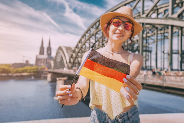 Chica feliz sosteniendo una bandera alemana contra el puente del Rin y la catedral de Colonia Dom. Lugares de interés turístico y fiestas tradicionales - Foto, imagen