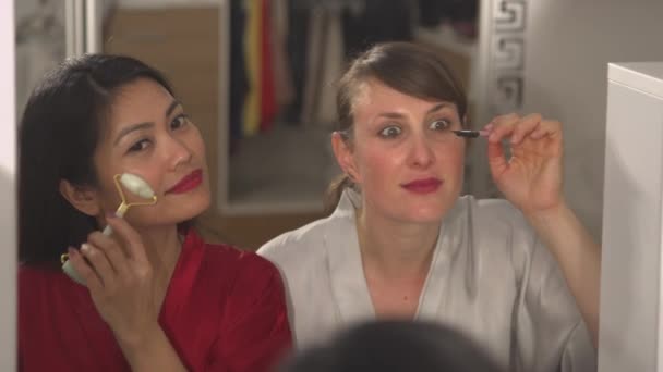 LEZÁRÁS Részletes kilátás a gyönyörű nők alkalmazó smink tükörreflexió. Kaukázusi és ázsiai nő használ szépségápolási termékek és készül egy éjszakát. Két hölgy, akinek szépségápolása van. - Felvétel, videó