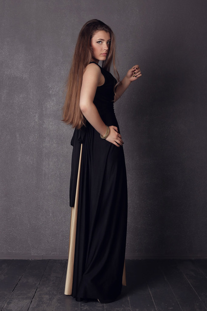 Young brunette lady in black ang golden dress posing on grey background - 写真・画像