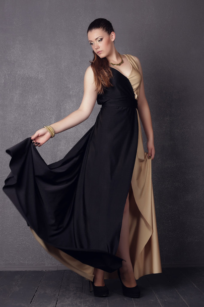 Young brunette lady in black ang golden dress posing on grey background - Foto, afbeelding