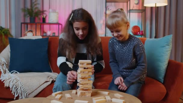 Tiener kind en kleine zus kind meisjes bouwen toren van houten bakstenen, verliezen bordspel concurrentie. broers en zussen kinderen of beste vrienden hebben plezier met toren op tafel, spelen met blokken thuis - Video