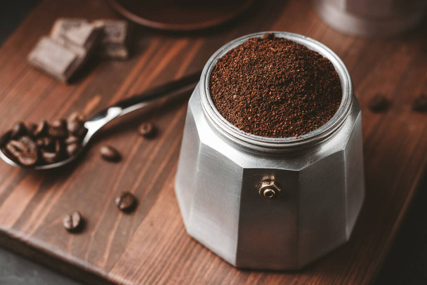 Moka koffiepot gevuld met bruine gemalen koffie op donker houten plank, voor te bereiden op het brouwen van Italiaanse espresso. - Foto, afbeelding
