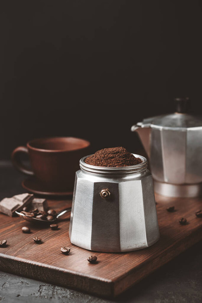 Moka cafetera llena de café molido marrón sobre tabla de madera oscura, prepararse para la elaboración de café espresso italiano. - Foto, Imagen