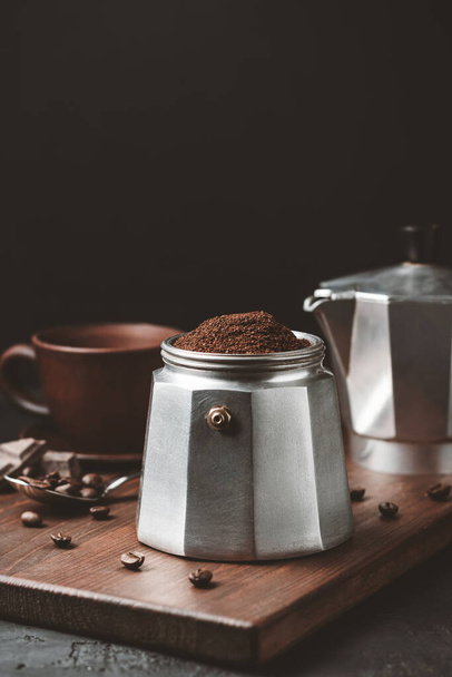 Moka cafetera llena de café molido marrón sobre tabla de madera oscura, prepararse para la elaboración de café espresso italiano. - Foto, Imagen