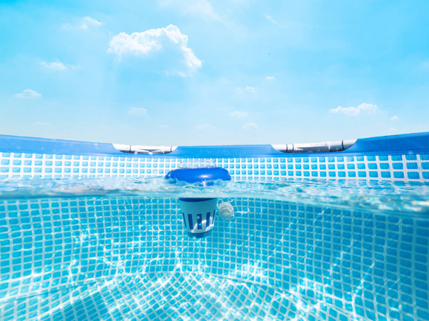 Dividere la vista subacquea di un distributore galleggiante di cloro in una piscina sotto un cielo blu - Foto, immagini