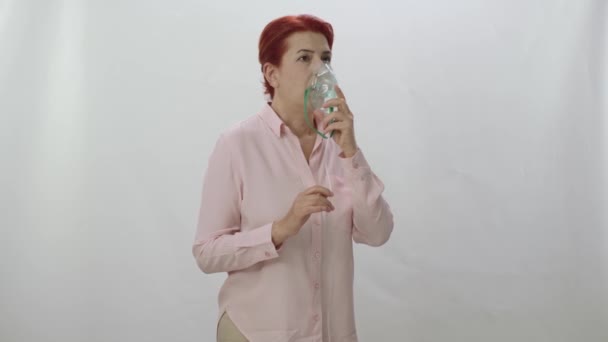 La mujer que sostiene un nebulizador enmascarado inhala la medicina del humo en sus pulmones. Mujer enferma respirando con máscara respiratoria, aislada sobre fondo blanco. Salud, medicina, cuidado, gripe, concepto de enfermedad. - Metraje, vídeo