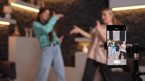 Weibliche Teenager tanzen zu Hause zusammen und nehmen ein Tanzvideo für die sozialen Medien mit der Smartphone-Kamera auf. Junge Blogger verschwimmen im Hintergrund, wenn sie Inhalte für ihren Kanal produzieren. Hochwertiges Filmmaterial. - Filmmaterial, Video