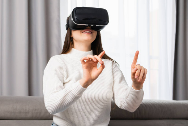 Felice giovane donna utilizzando un auricolare realtà virtuale e premendo pulsanti invisibili. - Foto, immagini