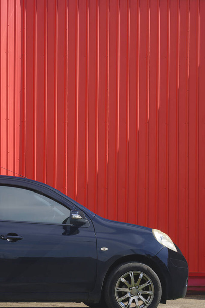 Egy fekete autó parkolt közelében piros hullámos acél fal belsejében szabadtéri parkoló terület függőleges keretben - Fotó, kép