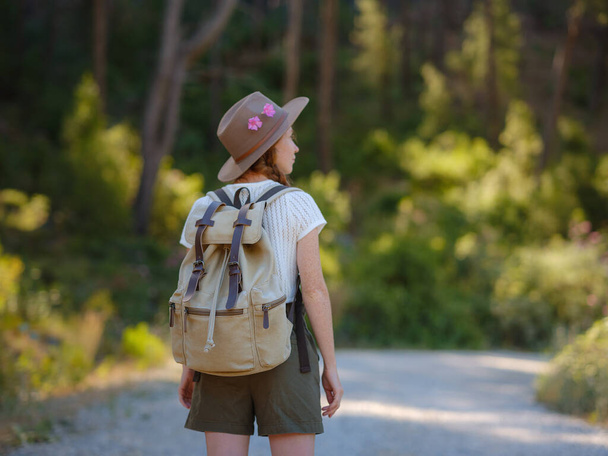 Καυκάσια κοκκινομάλλα νεαρή όμορφη γυναίκα σακίδιο που ταξιδεύει μόνη στο δάσος. Ελκυστική ταξιδιώτη ματιά γύρω και να εξερευνήσετε, ενώ τα πόδια στο ξύλο της φύσης με την ευτυχία και τη διασκέδαση κατά τη διάρκεια διακοπών ταξίδι. - Φωτογραφία, εικόνα