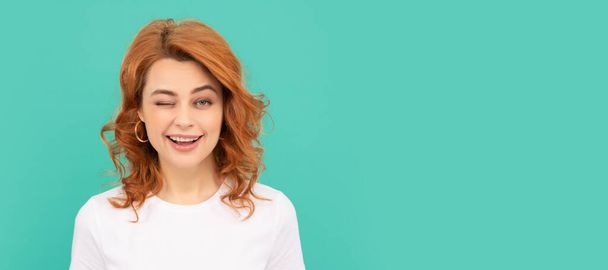 winking redhead woman with curly hair on blue background. Woman isolated face portrait, banner with copy space - Photo, Image
