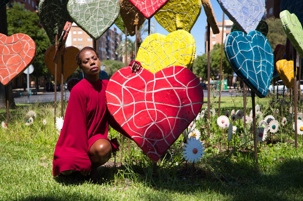 Young and beautiful Afro American woman hugging hearts of different sizes and colors in a park. Valentine's Day - Photo, Image