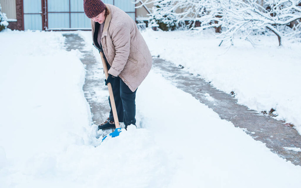 冬の問題の概念。庭でシャベルで雪を掘る女性。青いシャベルとクリーニング雪で立っている女性。冬のルーティンコンセプト - 写真・画像