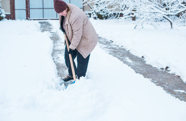 Talvi ongelmia käsite. Nainen kaivamassa lunta lapiolla pihalla. Lady seisoo sininen lapio ja puhdistus lunta.Winter rutiini käsite - Valokuva, kuva