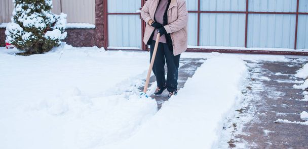 Conceito de problemas de inverno. Mulher cavando neve com pá no quintal. Senhora de pé com pá azul e limpeza de neve. Conceito de rotina de inverno - Foto, Imagem