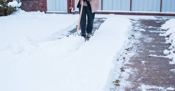 冬の問題の概念。庭でシャベルで雪を掘る女性。青いシャベルとクリーニング雪で立っている女性。冬のルーティンコンセプト - 写真・画像