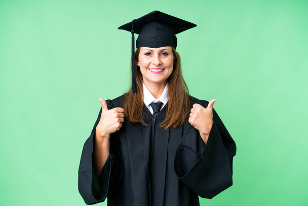 Középkorú egyetemi diplomás nő elszigetelt háttér hüvelykujj fel gesztus és mosolygós - Fotó, kép