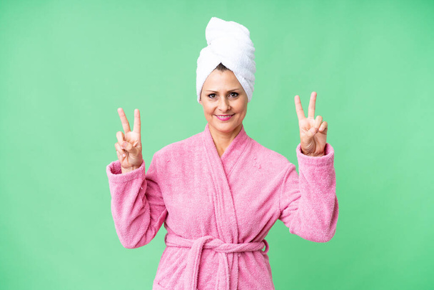 Middle age caucasian woman in a bathrobe over isolated background showing victory sign with both hands - Fotografie, Obrázek