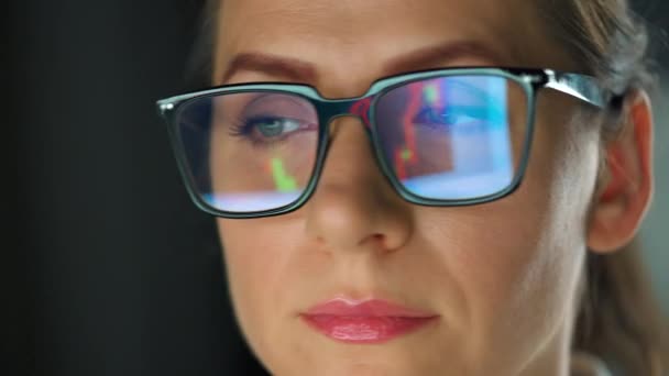 Een vrouw met een bril die op de monitor kijkt en werkt met grafieken en analyses. Het beeldscherm wordt gereflecteerd in de bril. Werk 's nachts. Extreme close-up. - Video