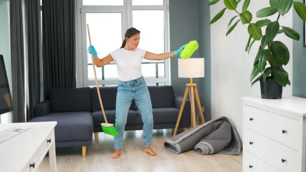 Blanke vrouw schoonmaken van het huis en plezier hebben dansen met een bezem en washandje - Video